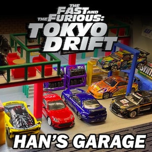 May include: A diorama of Han's Garage from The Fast and the Furious: Tokyo Drift. The scene features several miniature cars in a garage setting, with the movie's title prominently displayed. The cars are in various colors and designs.