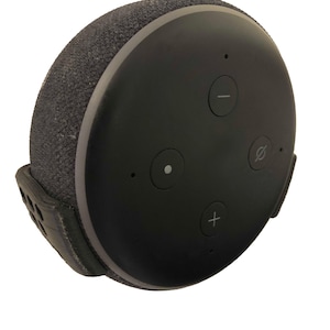 May include: A black and grey smart speaker with a fabric exterior and a silver ring around the top. The speaker has three buttons on the front: a plus sign, a minus sign, and a circle with a curved line through it.