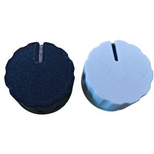 May include: Two round control knobs, one black and one white, with a textured surface and a vertical slot. These knobs are likely for electronic devices or audio equipment.