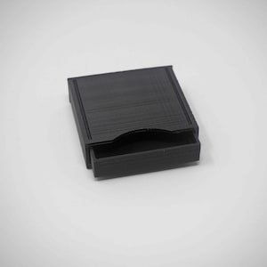 May include: A small black box with a drawer that slides open. The box is made of a textured plastic material.