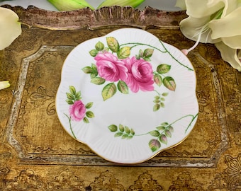 May include: A white porcelain plate with a scalloped edge features a pink rose floral design. The plate has a delicate, embossed pattern.