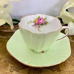 Könnte beinhalten: Ein hellgrünes Tee-Set mit Blumenmuster. Die Tasse hat einen gewellten Rand und die Untertasse ist quadratisch.