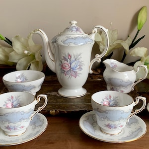 Peut inclure: Service à thé vintage avec un motif bleu clair et floral. L'ensemble comprend une théière, un pot à crème, un sucrier et plusieurs tasses à thé avec soucoupes. Des bordures dorées ornent les bords des tasses et des soucoupes. L'ensemble est disposé sur une surface en bois.