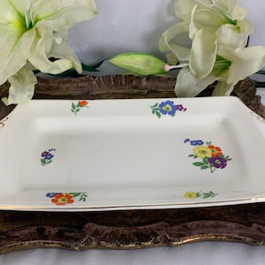 May include: A white rectangular serving platter with a gold trim and a floral design in shades of blue, yellow, orange, and green.
