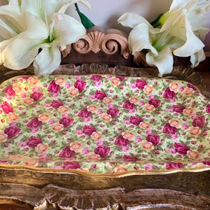 May include: A rectangular serving tray with a floral pattern of pink, yellow, and red roses on a green background. The tray has a gold rim and is made of ceramic.