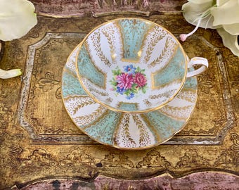 May include: A vintage teacup and saucer set with a delicate floral design and gold trim. The cup and saucer are both a light blue color with a white background. The floral design features pink, blue, and white flowers.
