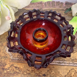 May include: A red glass candle holder with a lattice design. The holder has a round base and a central pillar for a candle.