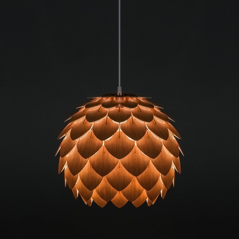 Pode incluir: Uma lumin&aacute;ria pendente com um design &uacute;nico. A l&acirc;mpada tem formato esf&eacute;rico, constru&iacute;da a partir de pain&eacute;is de madeira sobrepostos. Os pain&eacute;is s&atilde;o de cor castanho quente, e a luz brilha atrav&eacute;s das fendas, criando um brilho suave. A l&acirc;mpada pende de um cabo branco.