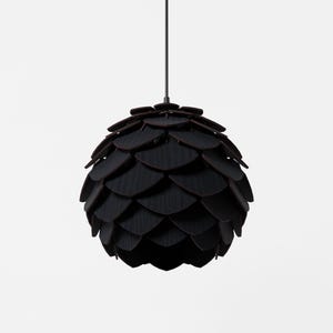 Könnte beinhalten: Eine schwarze Pendelleuchte mit einem geschichteten, blütenblattartigen Design. Die Leuchte hängt an einem schwarzen Kabel und hat einen dunkelbraunen Rand an jedem Blütenblatt. Die Gesamtform ähnelt einem Tannenzapfen. Diese dekorative Leuchte ist für jeden Raum geeignet.