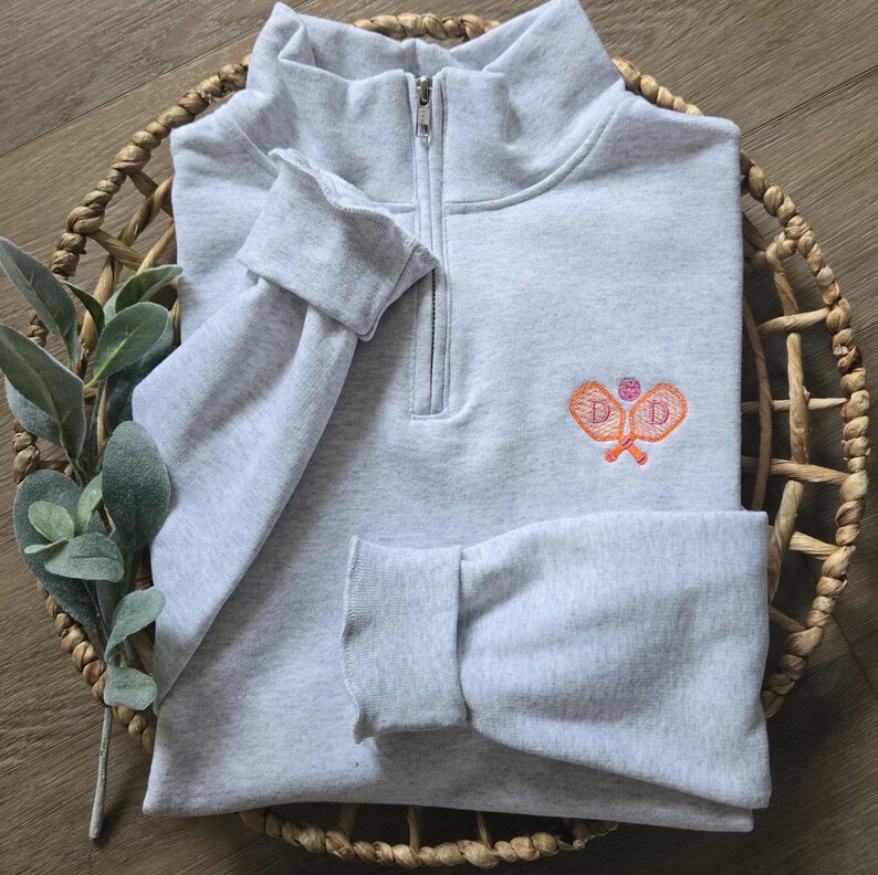 An ash quarter zip with orange for the paddles and pink for the pickleball and initials.