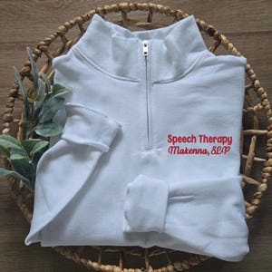Pu&ograve; includere: Felpa bianca con zip a un quarto con testo ricamato in rosso che recita "Speech Therapy Makenna, SLP".