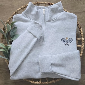 An ash sweatshirt with navy thread for the paddles/initials and caramel thread for the ball.