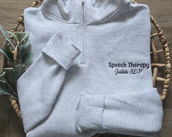 May include: Gray quarter-zip sweatshirt with the text "Speech Therapy Julia SLP" embroidered on the front.