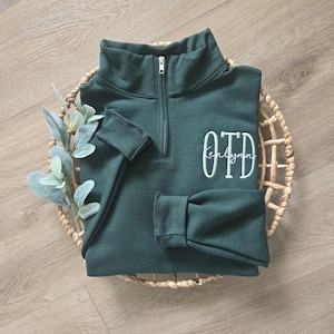 A forest green sweatshirt with sea foam green thread for OTD and white thread for the name.