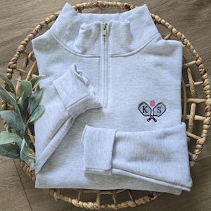 An ash sweatshirt with navy thread for the paddles and initials, and pink thread for the pickleball.