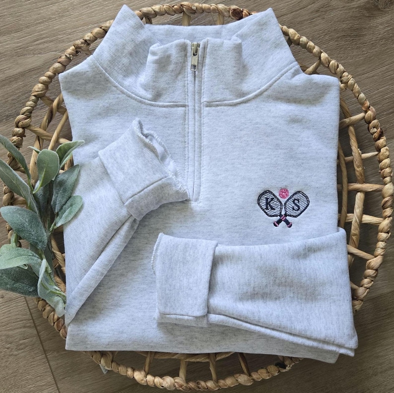 An ash sweatshirt with navy thread for the paddles and initials, and pink thread for the pickleball.