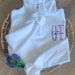 May include: White quarter-zip sweatshirt with a purple embroidered "OT Katie" design.