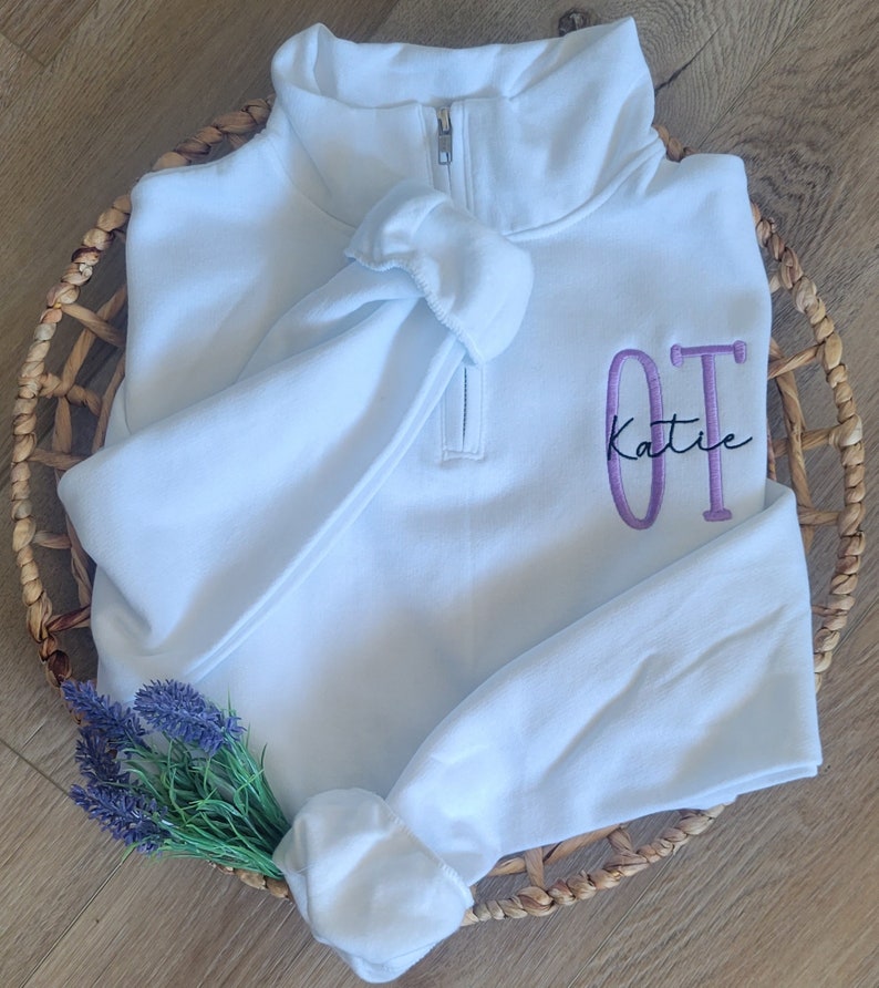 May include: White quarter-zip sweatshirt with a purple embroidered "OT Katie" design.