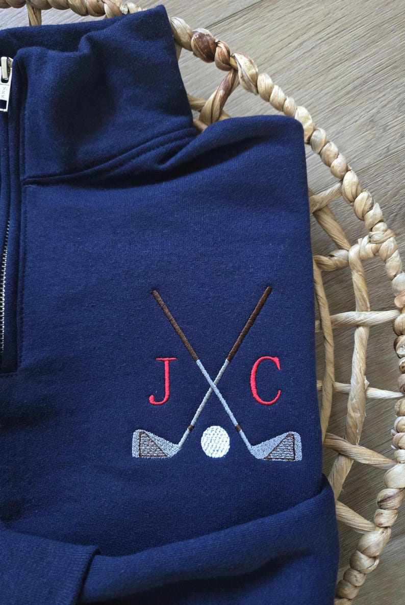 Peut inclure: Sweat-shirt bleu marine avec une fermeture &eacute;clair quart de zip. Il pr&eacute;sente un motif brod&eacute; de clubs de golf crois&eacute;s, d'une balle de golf et des lettres "J" et "C" en rouge. Le sweat-shirt est en mati&egrave;re douce.