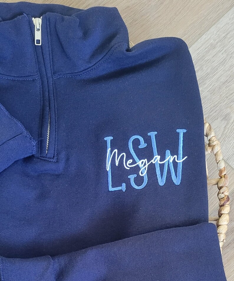May include: A navy blue quarter-zip sweatshirt with a white embroidered name "Megan" and blue embroidered initials "L.S.W."