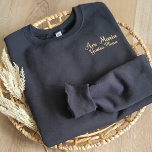 May include: Black sweatshirt with gold embroidery that reads "Ave Maria Gratia Plena".