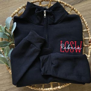 May include: Black quarter-zip sweatshirt with a red embroidered monogram that says "LCSW Rebecca"