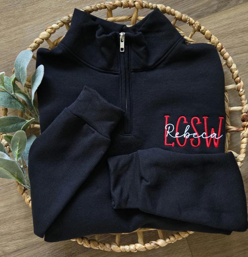 May include: Black quarter-zip sweatshirt with a red embroidered monogram that says "LCSW Rebecca"
