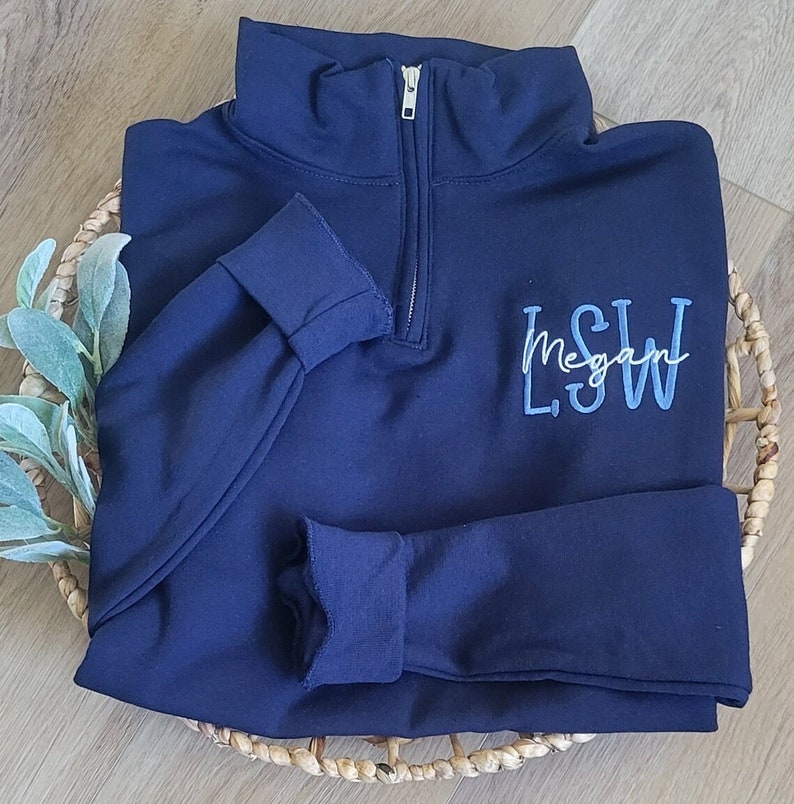 May include: A navy blue quarter-zip sweatshirt with a blue embroidered monogram that reads "L.S.W. Megan".