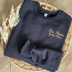 May include: Black sweatshirt with gold embroidery that reads "Ave Maria Gratia Plena".