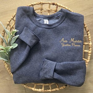 May include: A dark blue sweatshirt with the text "Ave Maria Gratia Plena" embroidered in gold on the front.