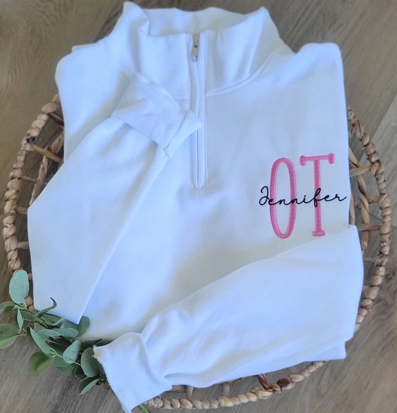 May include: White quarter-zip sweatshirt with a pink embroidered "OT" and the name "Jennifer" in black script.
