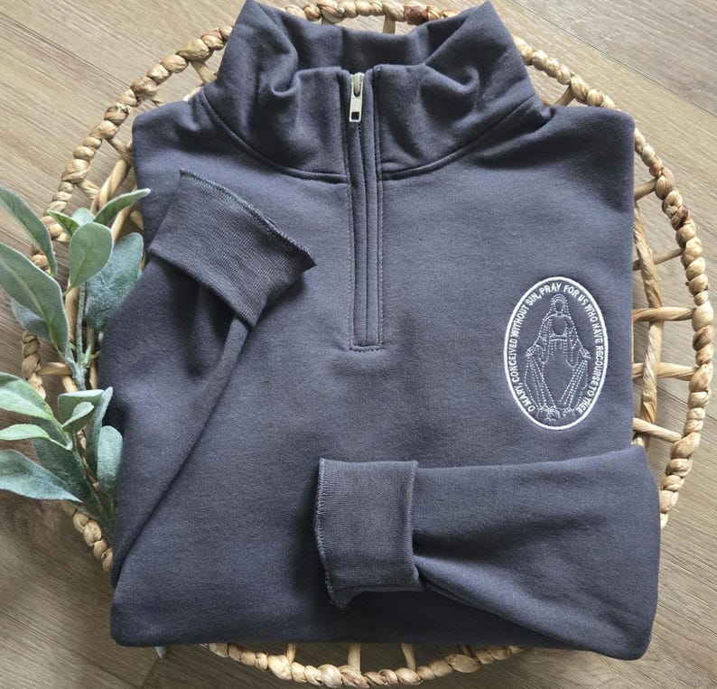 A charcoal greay sweatshirt with white thread for the miraculous medal.