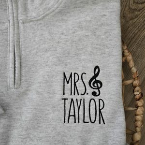 May include: Gray zippered sweatshirt with black embroidered text that reads "MRS. TAYLOR" with a treble clef symbol.