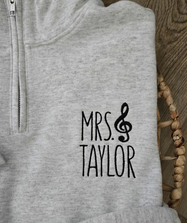 May include: Gray zippered sweatshirt with black embroidered text that reads "MRS. TAYLOR" with a treble clef symbol.