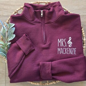 May include: Burgundy quarter-zip sweatshirt with white embroidered text "MRS. &" and "MACKENZIE".