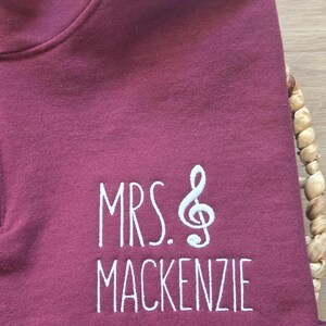 May include: Burgundy colored sweatshirt with white embroidery that reads "MRS. &" with a treble clef symbol and "MACKENZIE".