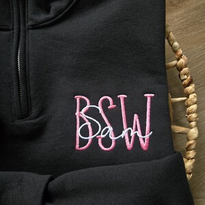 May include: Black quarter-zip sweatshirt with pink embroidered letters "BSW" and a smaller white embroidered word "Sam" below.
