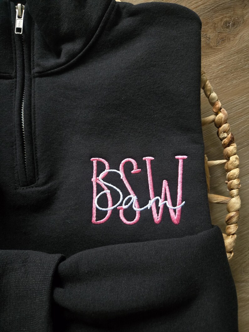 May include: Black quarter-zip sweatshirt with pink embroidered letters "BSW" and a smaller white embroidered word "Sam" below.