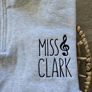 May include: Gray zippered sweatshirt with the text "Miss Clark" and a musical note embroidered on the front.