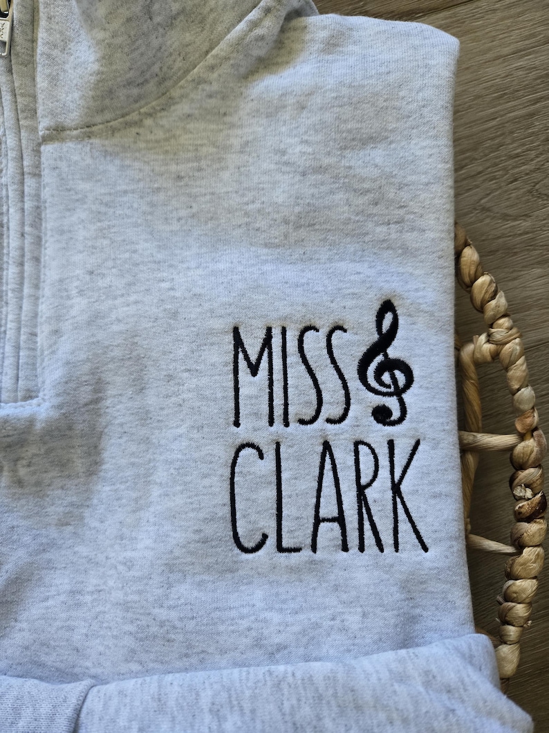 May include: Gray zippered sweatshirt with the text "Miss Clark" and a musical note embroidered on the front.