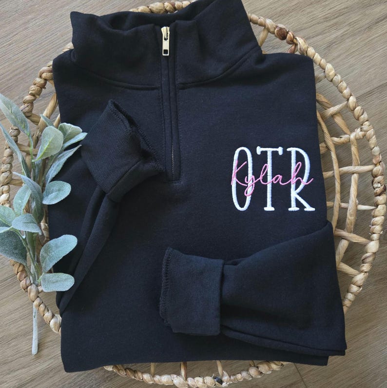 A black sweatshirt with white thread for OTR and pink thread for the name.