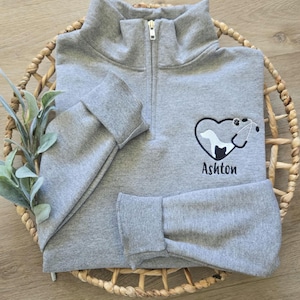 May include: Gray quarter-zip sweatshirt with a heart design featuring a dog and cat inside, a stethoscope, and the name "Ashton" embroidered on the front.