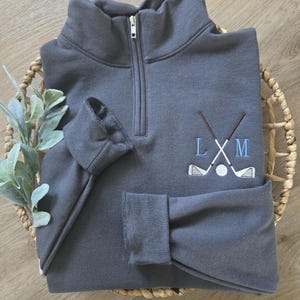 A charcoal grey quarter zip with sky blue thread for the initials.