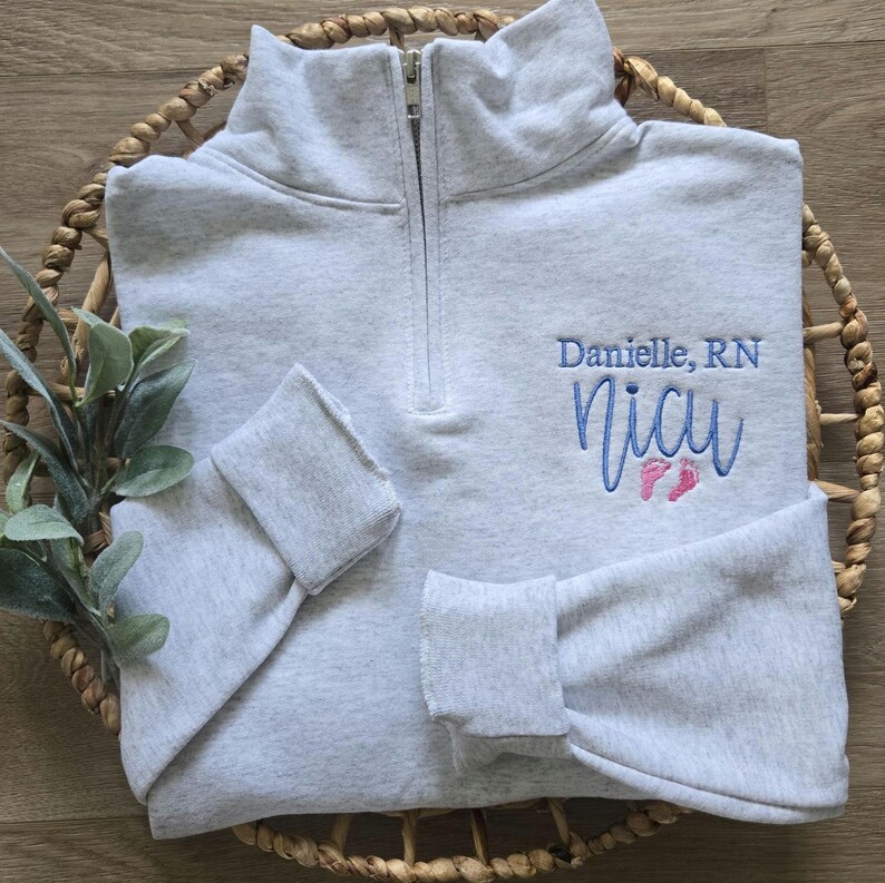 An ash sweatshirt with sky blue thread for the name/NICU and pink thread for the feet.