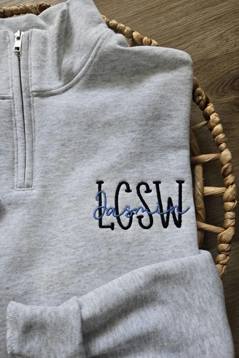 May include: A grey quarter-zip sweatshirt with the name "Jasmine" embroidered in blue and black lettering.