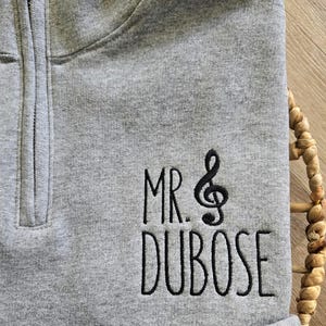May include: Gray quarter-zip sweatshirt with black embroidered text that reads "MR. & DUBOSE" with a treble clef symbol.