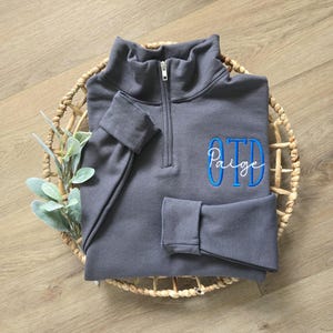 A charcoal grey sweatshirt with blue thread for OTD and white thread for the name.