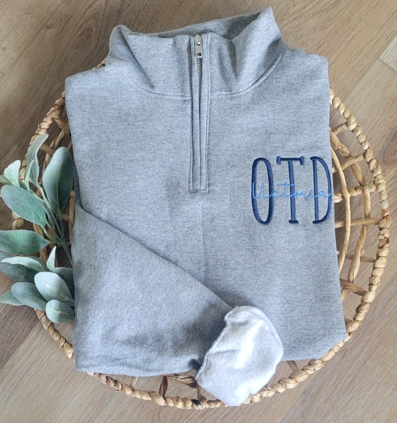 May include: A grey quarter-zip sweatshirt with a blue embroidered monogram that says "OTD".