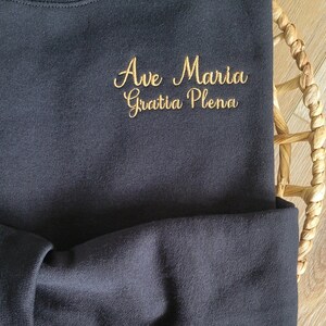 May include: Black sweatshirt with gold embroidery that reads "Ave Maria Gratia Plena".