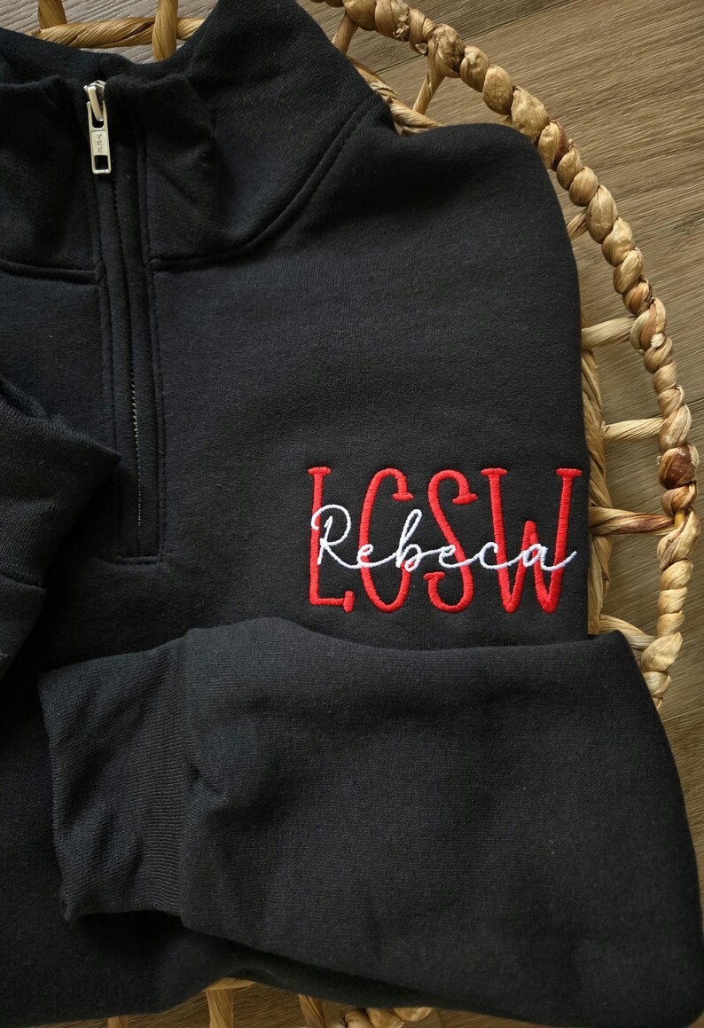 May include: Black quarter-zip sweatshirt with red embroidered lettering that says "LCSW Rebecca".